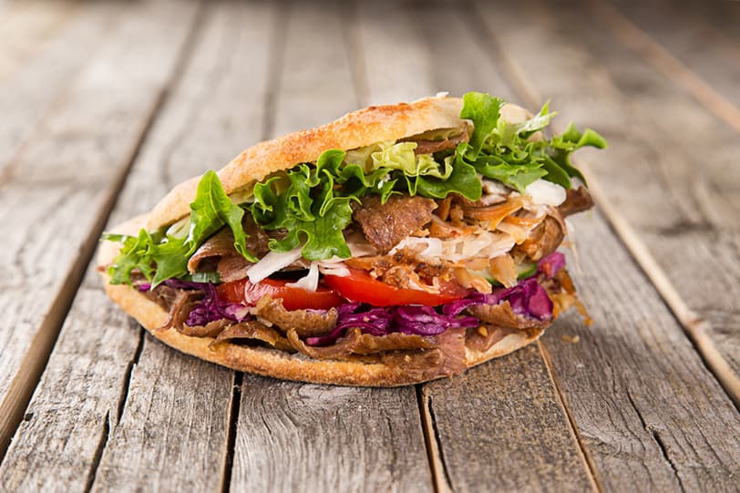 Ein Döner im aufgeschnittenen Fladenbrot: Die Tasche steht oben offen, Fleisch, Salat, Tomate und Rotkohl schauen heraus.
