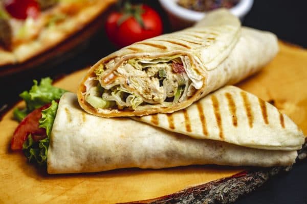 Zwei gerollte Dürüm auf einem Holzbrett, einer quer angeschnitten; im Anschnitt sind Fleisch und Salat zu sehen, umschlossen von einer durchgehenden Lage Fladen.